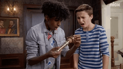 two boys are standing next to each other in a room and one of them is holding a gold object .