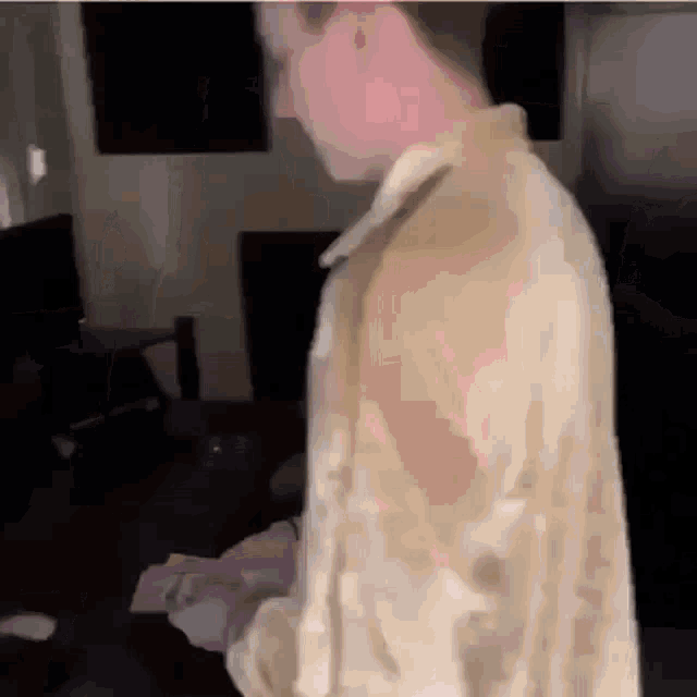 a man in a tan jacket is standing in a living room holding a piece of paper .