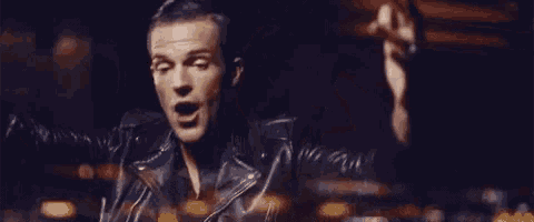 a man in a leather jacket is standing in a dark room with his hands outstretched and his mouth open .