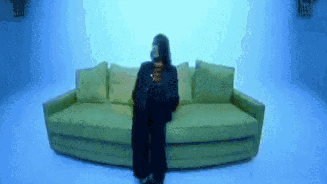 a woman in a black coat is sitting on a green couch in a blue room .