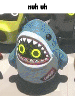 a stuffed shark with yellow eyes and teeth is sitting on a table .
