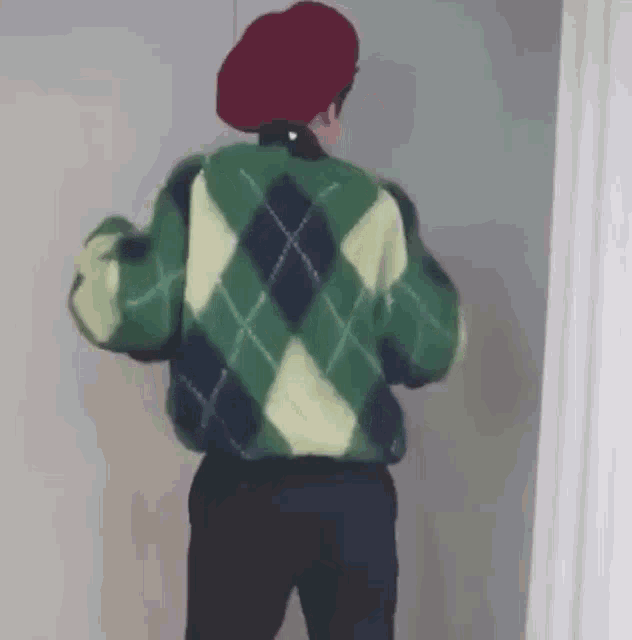 a man wearing a green sweater and a red beret is standing in front of a door .