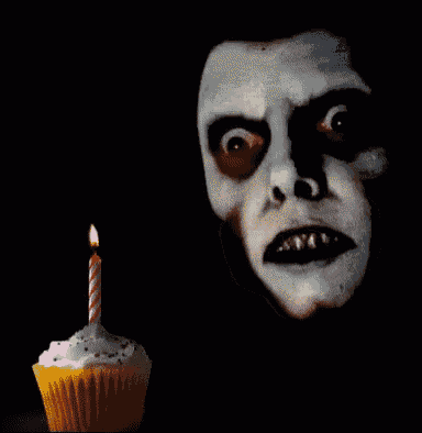 a cupcake with a lit candle in front of a skeleton face