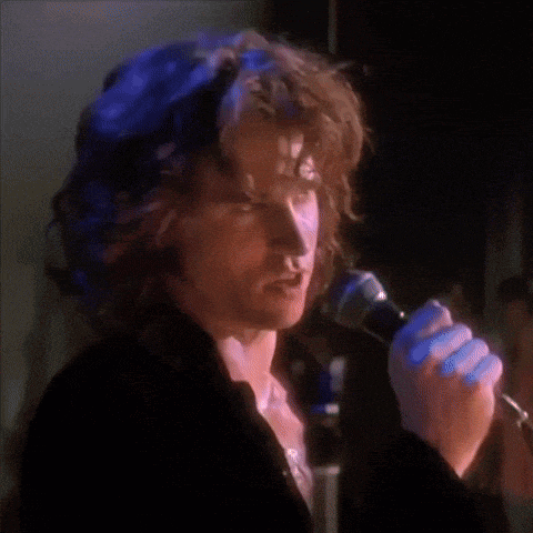 a man with long hair is singing into a microphone
