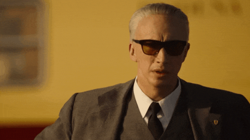 a man wearing sunglasses and a suit has a ferrari badge on his jacket