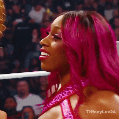 a woman with pink hair is smiling and holding a wrestling championship belt .