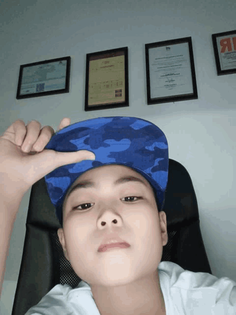 a boy wearing a blue hat is sitting in front of framed certificates