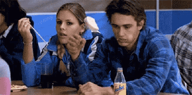 a man and a woman are sitting at a table with a fanta bottle
