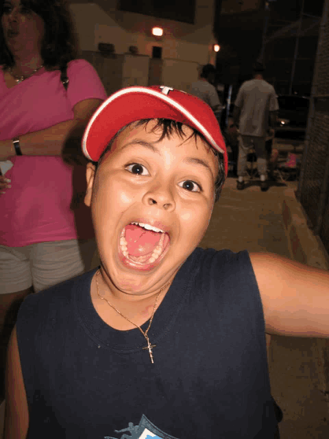 a young boy wearing a red hat with the letter t on it is making a funny face