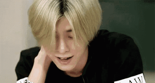 a young man with blonde hair is crying while holding his neck .
