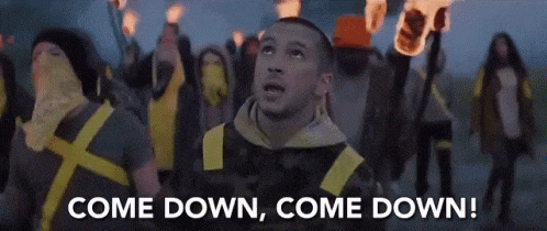 a man is standing in front of a group of people holding torches and a sign that says come down come down .