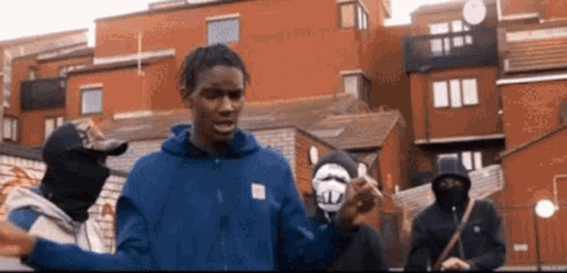 a group of men are standing in front of a brick building . one of the men is wearing a blue hoodie .
