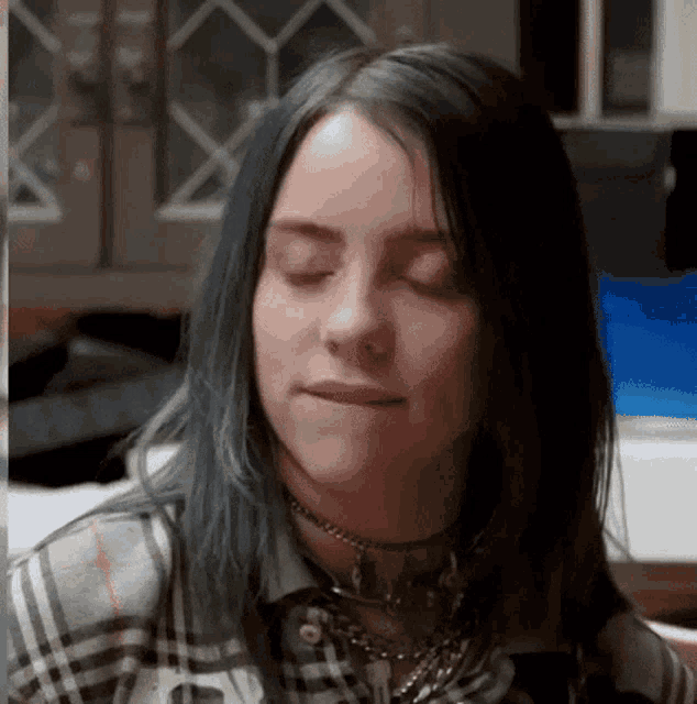 billie eilish is wearing a plaid shirt and a choker necklace .