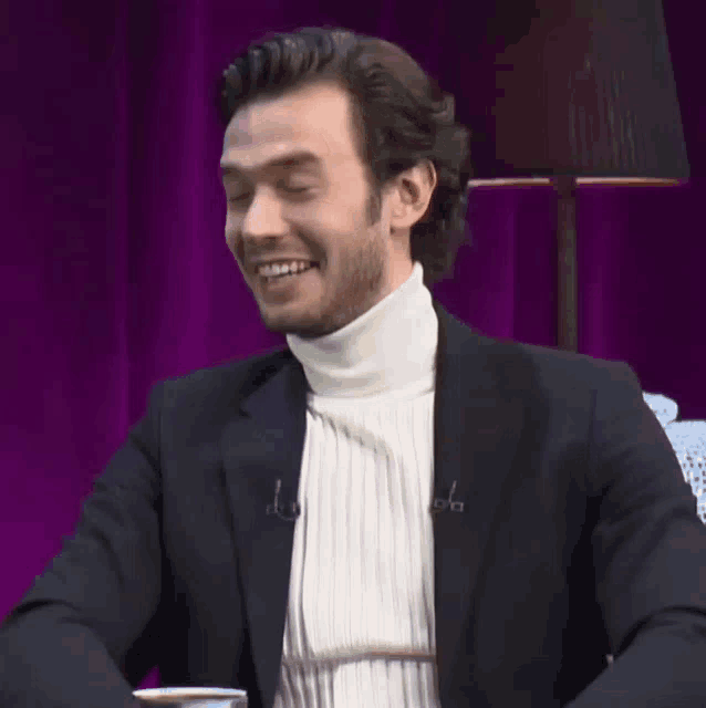 a man wearing a white turtleneck and a black jacket is smiling with his eyes closed
