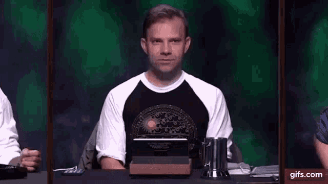 a man wearing a black and white shirt is sitting in front of a green background .