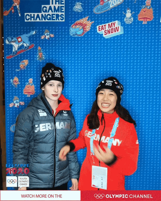 a girl in a red jacket stands next to a boy in a gray jacket in front of a sign that says the game changer