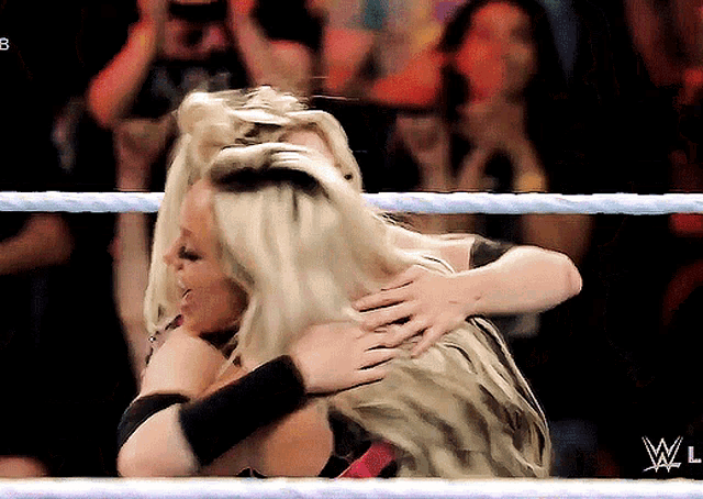 two women hugging in a wrestling ring with a w logo on the bottom right