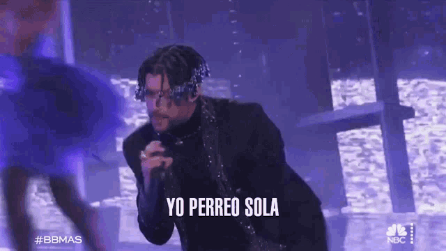 a man in a suit singing into a microphone with yo perreo sola written above him