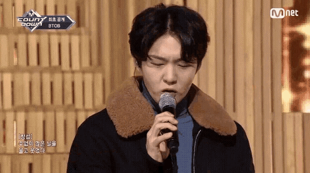 a young man singing into a microphone with a mnet logo behind him