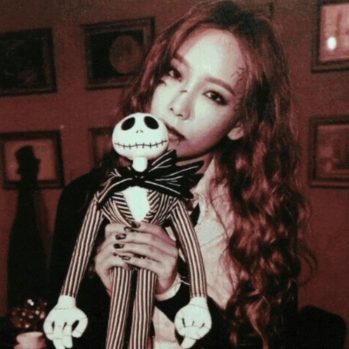 a woman with a tattoo on her face is holding a jack skellington doll
