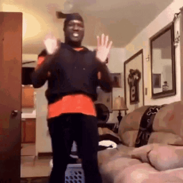 a man is standing in a living room with his hands in the air .