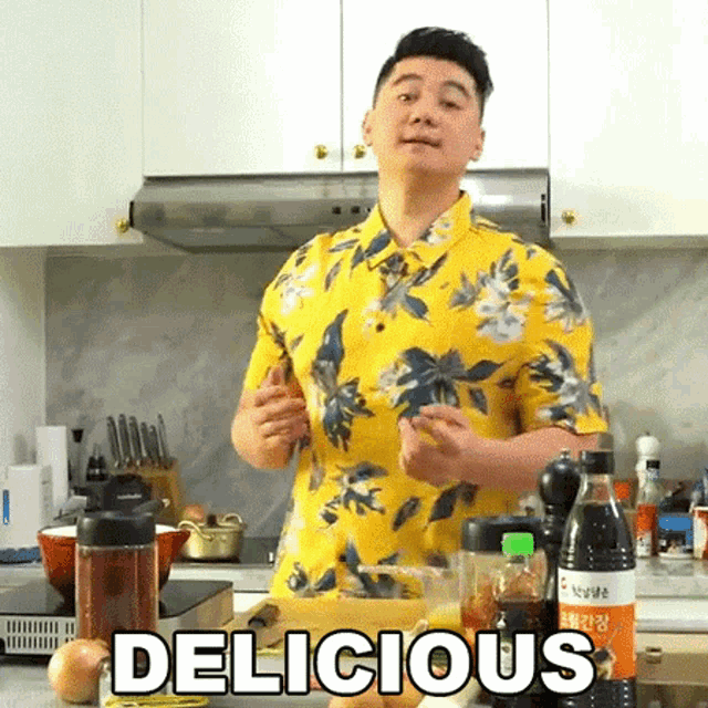 a man in a yellow shirt is standing in a kitchen with the word delicious written on the counter .
