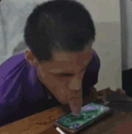 a man in a purple shirt is licking a cell phone with his tongue .
