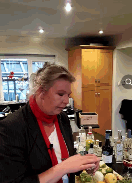 a woman in a red scarf holds a glass in front of a table full of bottles
