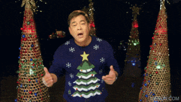 a man wearing a blue sweater with a christmas tree on it is giving a thumbs up