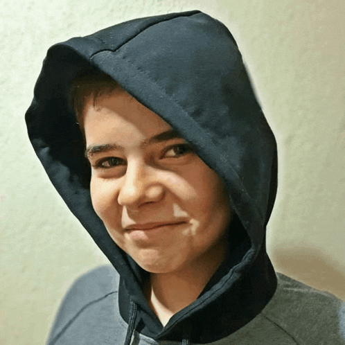 a young boy wearing a black hooded sweatshirt smiles for the camera