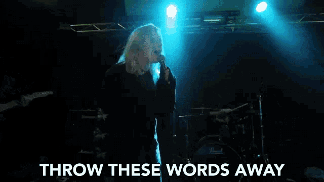 a woman singing into a microphone with the words " throw these words away " behind her