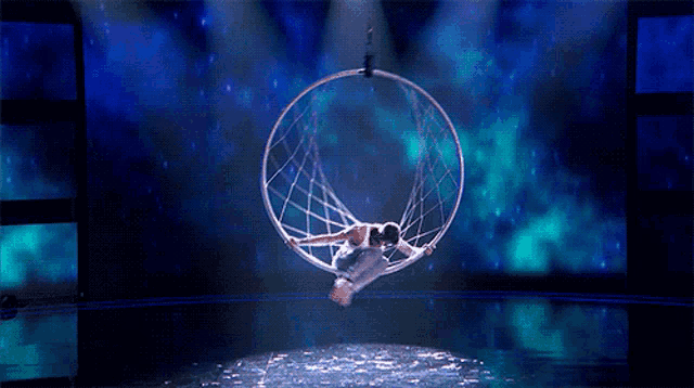 a woman in a white dress is hanging upside down in a hoop on a stage