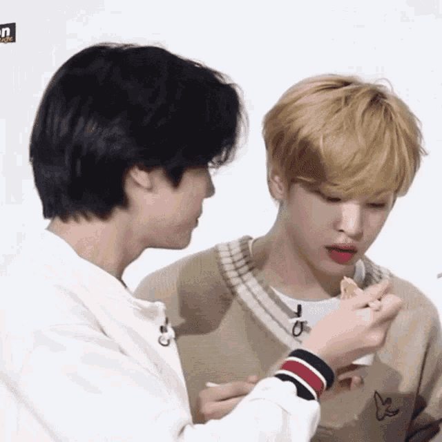 a man is feeding another man a piece of food while they are sitting next to each other .