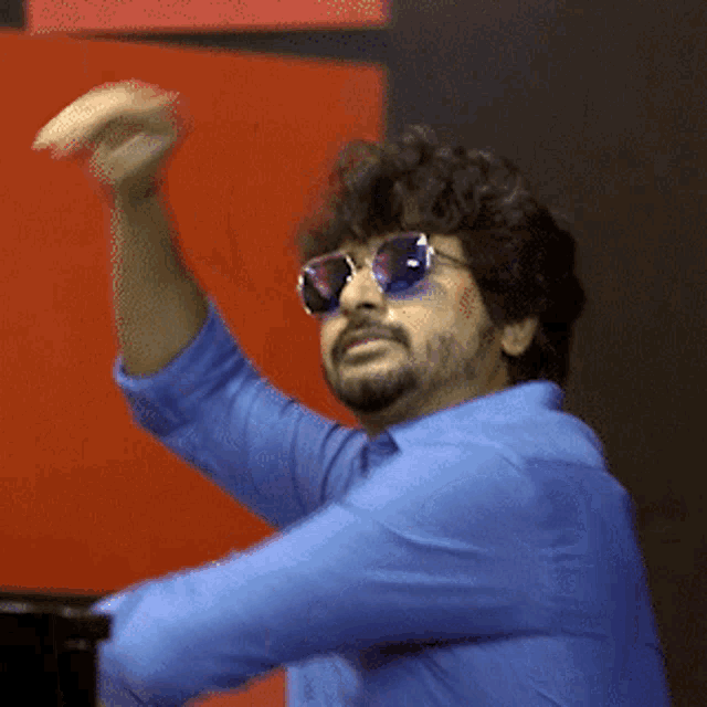 a man wearing sunglasses and a blue shirt is raising his arm in the air