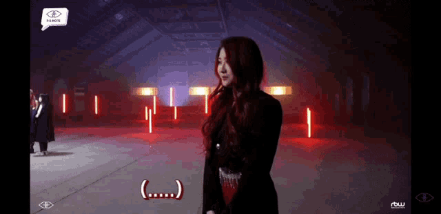 a woman is standing in a dark room with red lights behind her