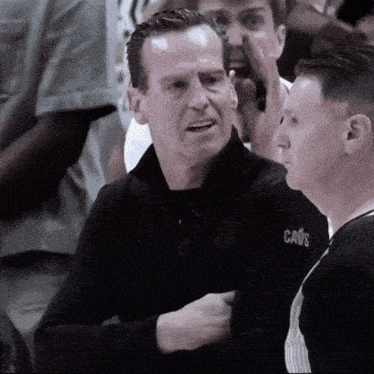 a man wearing a cavs jacket talks to a referee