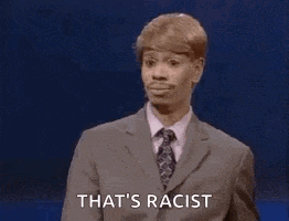 a man in a suit and tie is standing in front of a blue background and saying that 's racist .