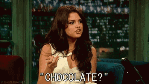 a woman is sitting on a couch eating a piece of chocolate and asking " chocolate ? "
