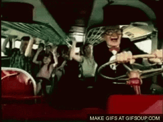 a man in a suit is driving a bus with a crowd of people on it .