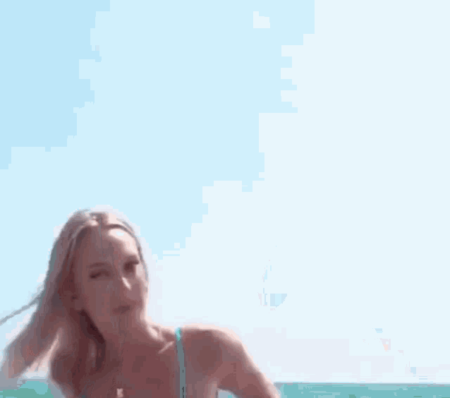 a woman in a bikini is standing in front of a blue sky and holding her hair .