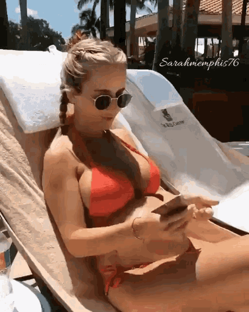 a woman in a red bikini is sitting on a lawn chair looking at her phone ..