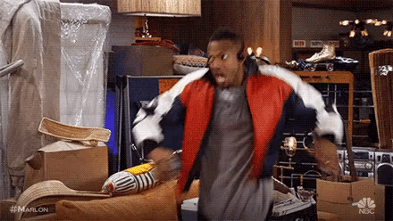 a man in a red jacket is dancing in a room filled with boxes and boxes .