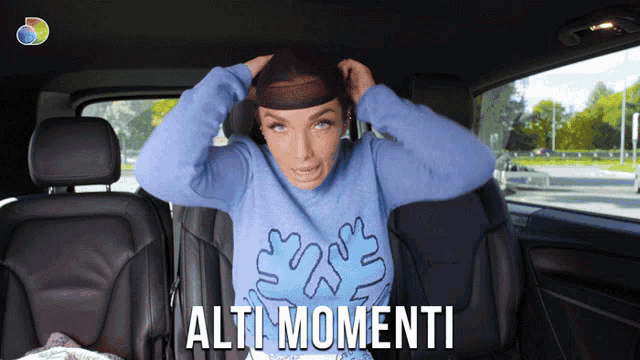 a woman in a blue sweater is sitting in a car with the words alti momenti on the bottom