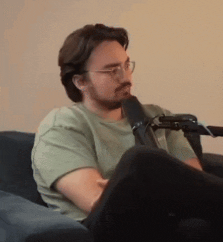a man with glasses and a beard is sitting in a chair in front of a microphone .