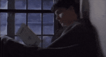 a man sitting in front of a window reading a book