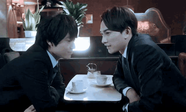 two men are sitting at a table with cups of coffee on it