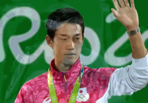 a man in a pink jacket with a medal around his neck is waving his hand in front of a sign that says rio