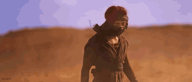 a woman with a turban on her head is standing in the desert .