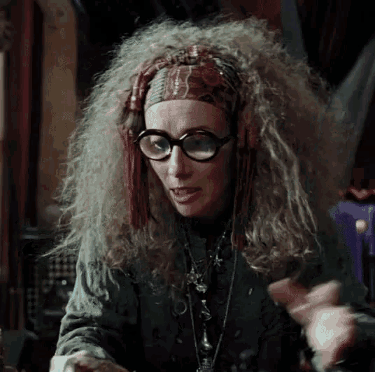 a woman with curly hair wearing glasses and a headband looks at the camera