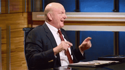 a man in a suit and tie is sitting at a desk with his hands in the air .